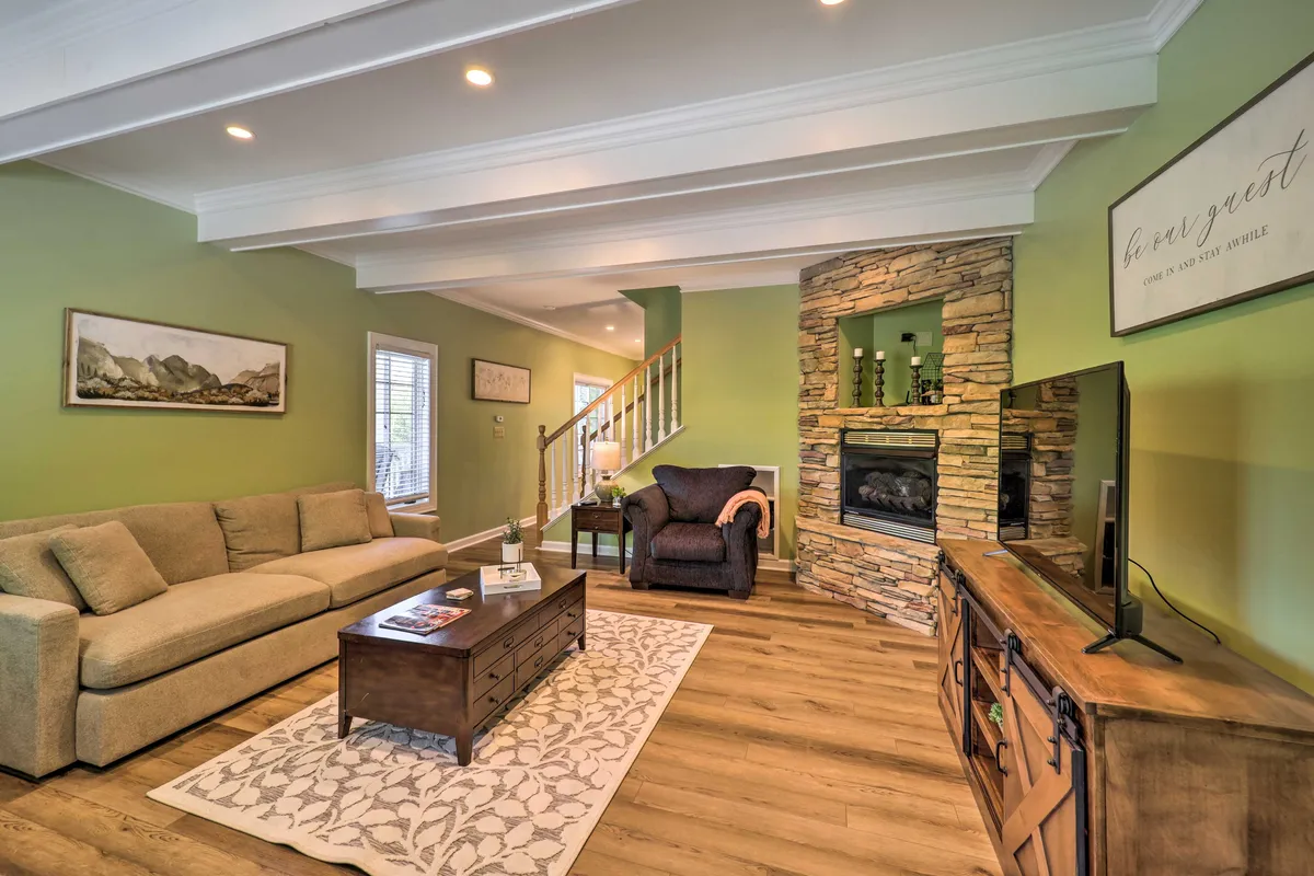 A warm, inviting living room featuring a comfortable sofa and armchair arranged around a gas log fireplace. The coffee table sits in front, and a large TV is mounted above the fireplace, with soft lighting enhancing the cozy atmosphere. The open layout hints at adjacent spaces, promoting connection and togetherness.