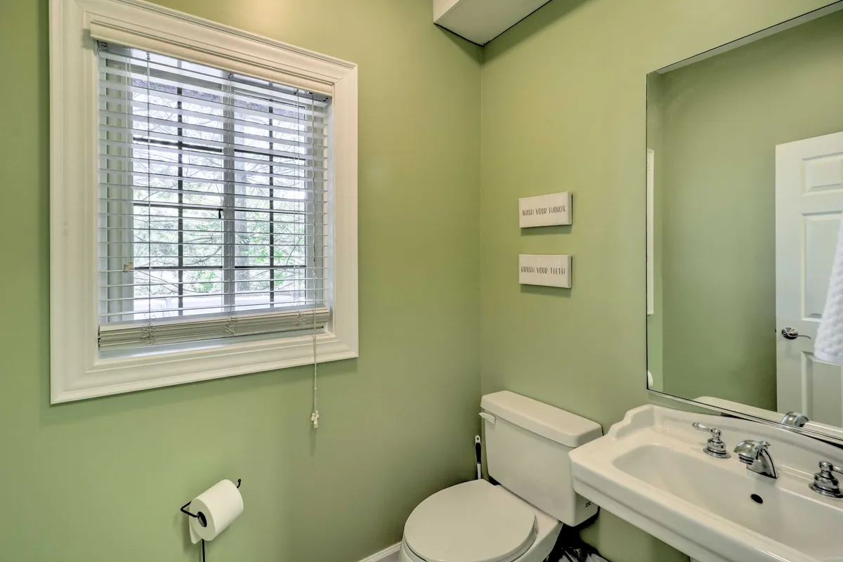 A bright bathroom featuring a classic sink, mirror, toilet, and a window for natural light. The space is tidy and serene, suggesting a welcoming spot for daily routines and guest convenience.
