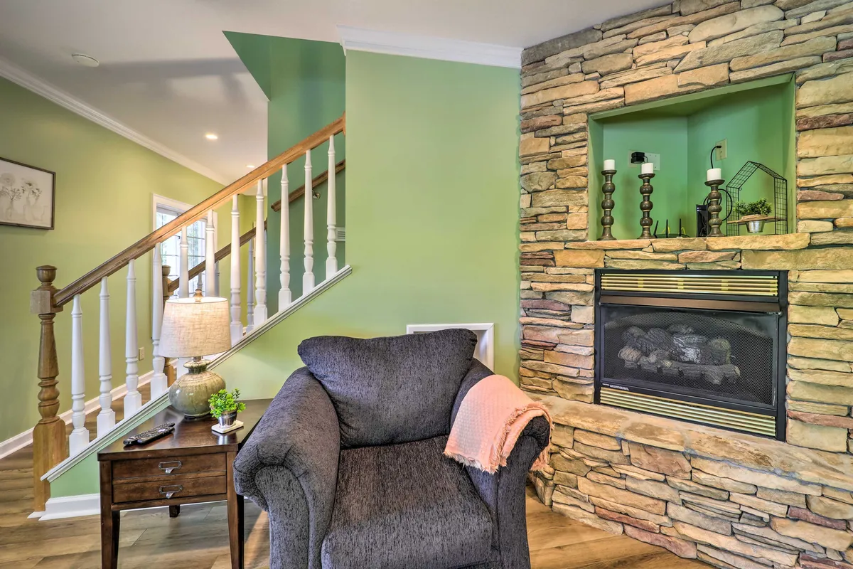 A cozy, welcoming living area with a roaring fireplace, a comfortable armchair, and a staircase leading up. The setting invites guests to relax after a day outside, suggesting warmth and camaraderie post-adventure.