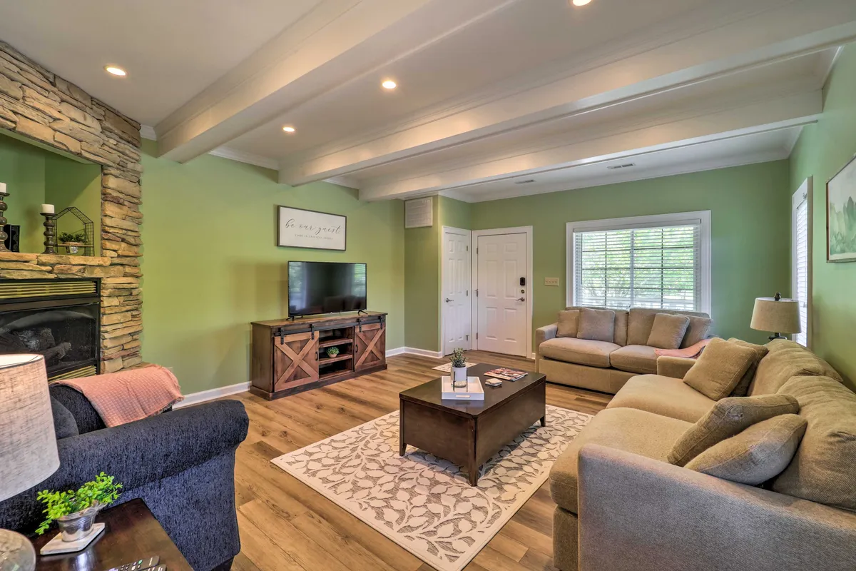 A view of a spacious and cozy living area with a stone fireplace, TV unit, and a plush sofa set. The coffee table sits at the center, inviting board games or shared snacks. The overall mood is one of warmth, ideal for socializing or unwinding together.