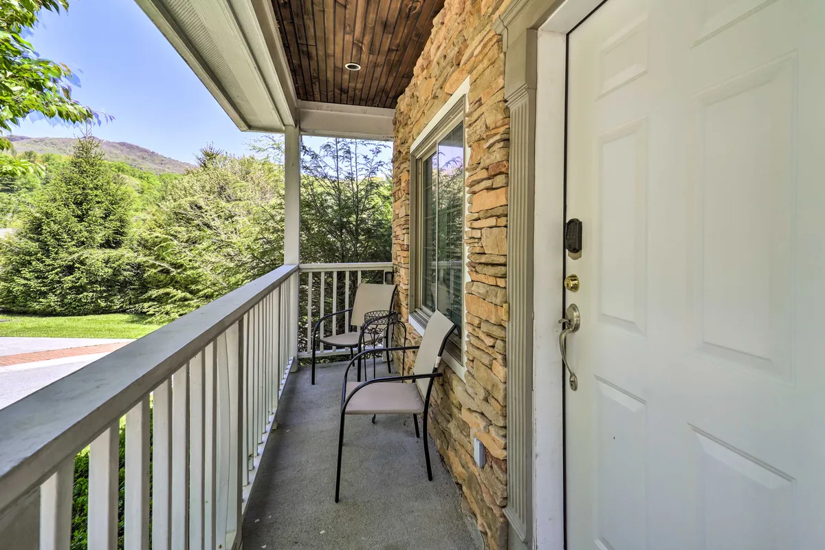 This exterior image showcases the front entrance of Lilly’s Mountain Escape, featuring a welcoming front door set into a stone wall, comfortable chairs, and a balcony railing. The setting is surrounded by morning sunlight and natural landscapes, communicating both practicality and the adventure-ready spirit.