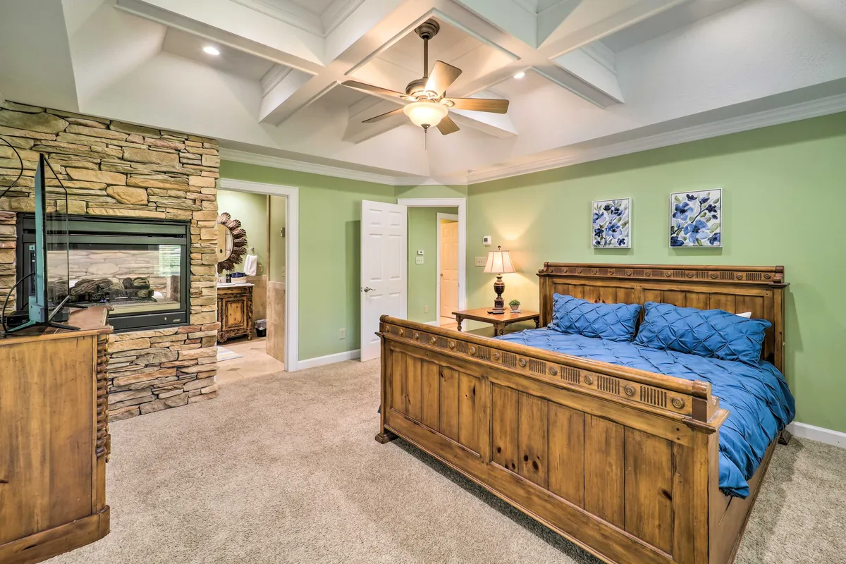 A serene king bedroom featuring a wooden bed with blue bedding, a fireplace, and elegant wall art. The space looks calm and well-appointed, suggesting comfort and relaxation. Soft lighting enhances the tranquil mood, and a plush chair invites quiet moments.