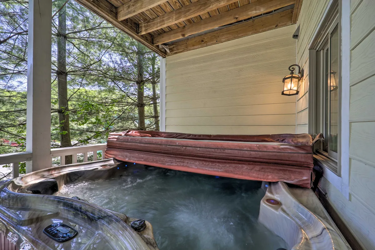 An exterior view of the hot tub area on the wooden deck, surrounded by greenery and supported by sturdy wooden beams. The hot tub is positioned for privacy and offers an immersive nature experience, ideal for stargazing or relaxing after a day of adventure.