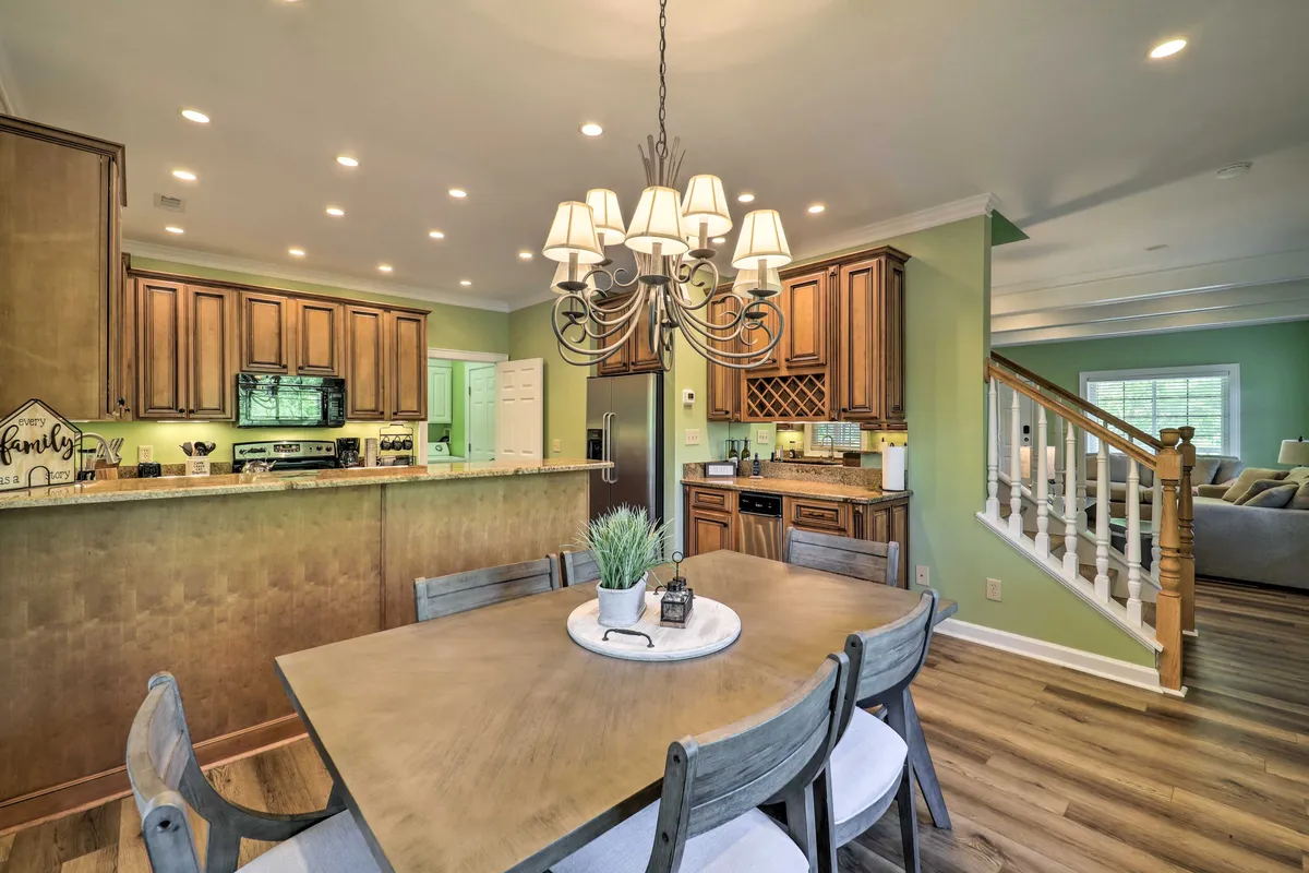 A bright, open-concept kitchen and dining area with a dining table, elegant chandelier, and custom cabinetry. Stainless steel appliances and granite counters highlight the kitchen's functionality and style. The space flows seamlessly into the living area, supporting communal meals or casual gatherings.