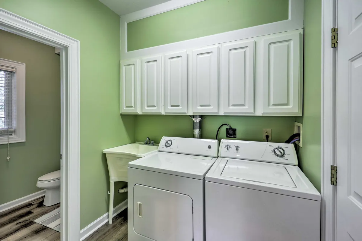 A bright, practical laundry area with washer, dryer, white cabinetry, green walls, and a sink, indicating thoughtful amenities for longer stays and year-round use.